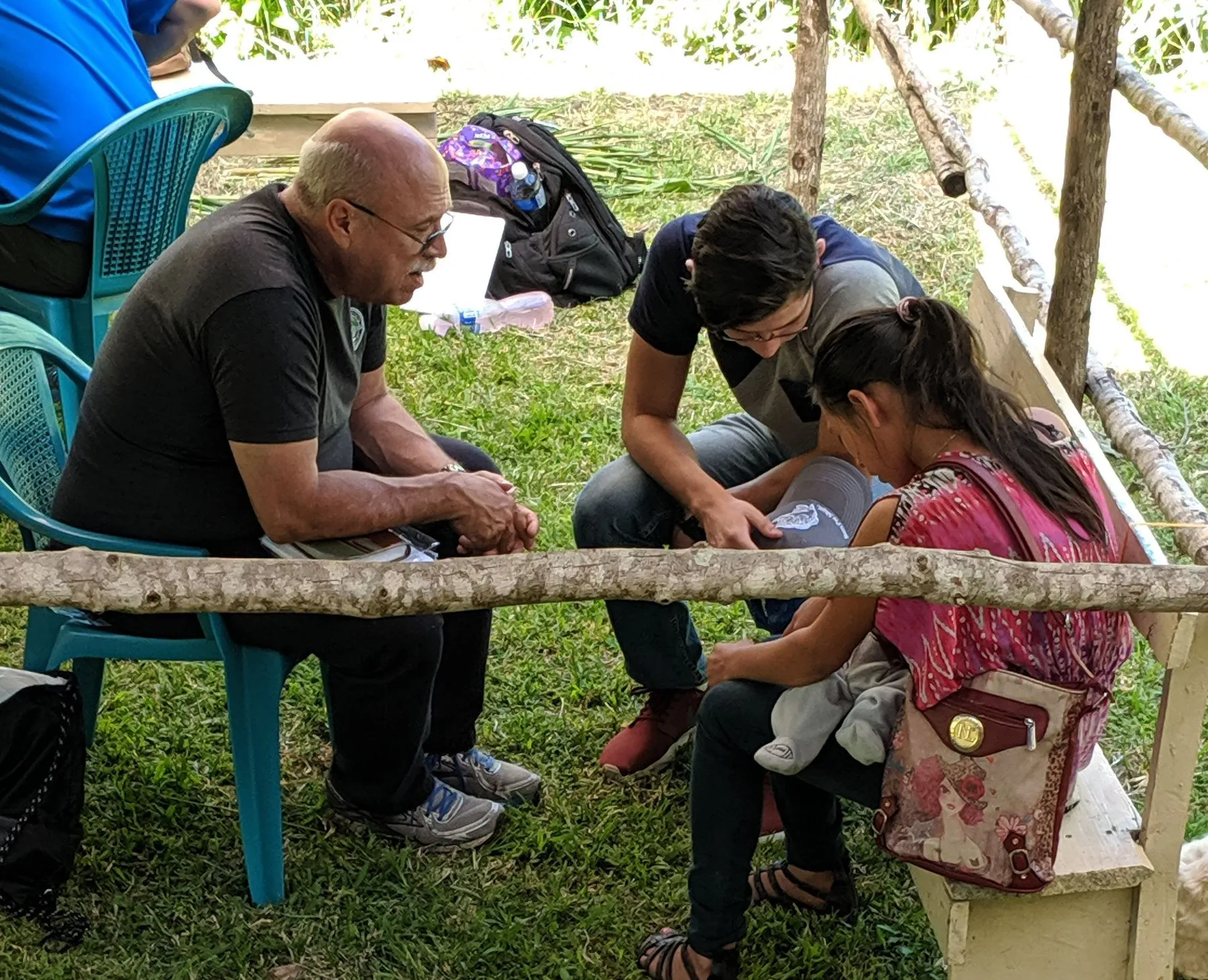 Paul seated under a tree praying with a woman and her child in Honduras.